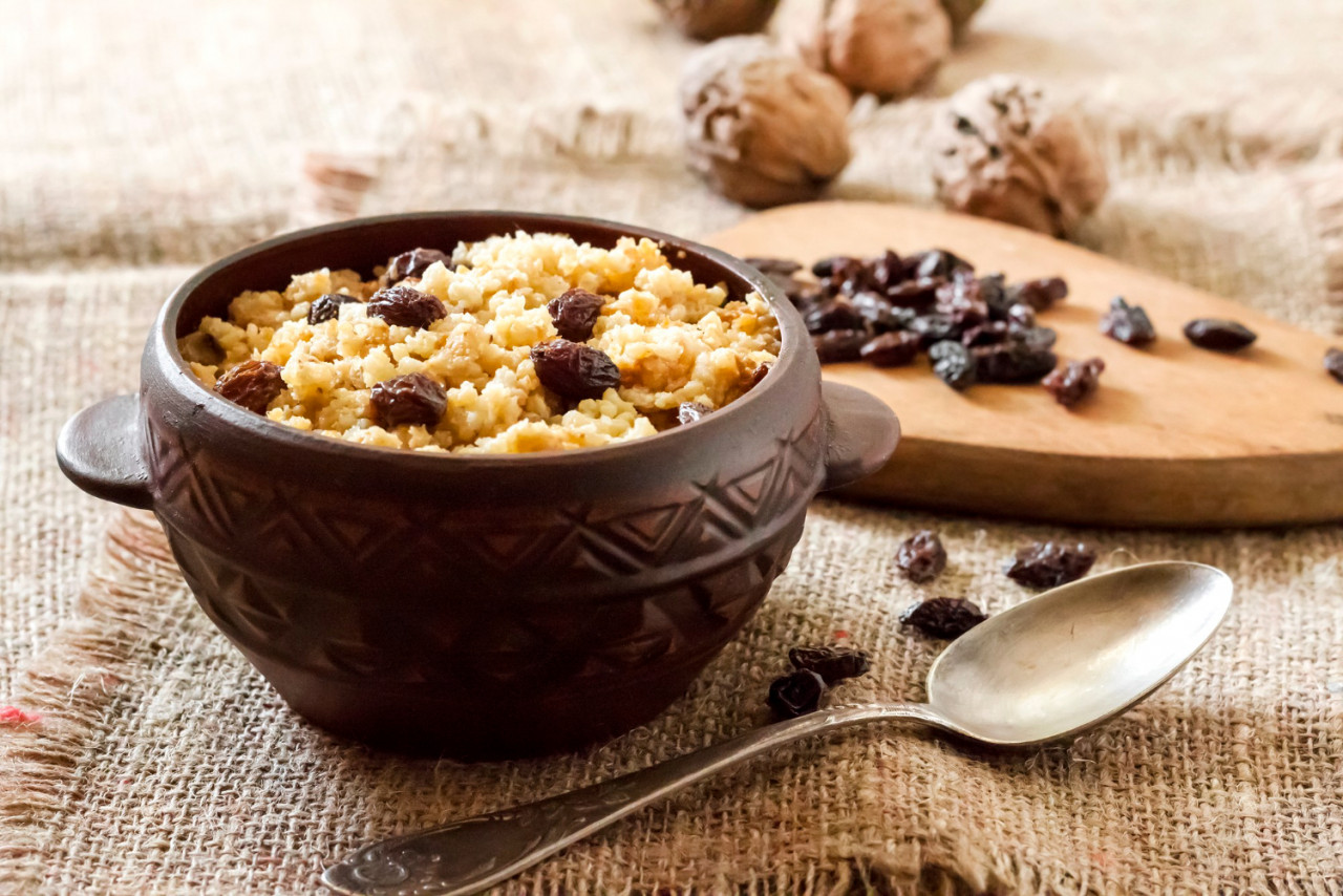 sweet millet porridge with dark raisins ceramic rustic bowl with walnuts background