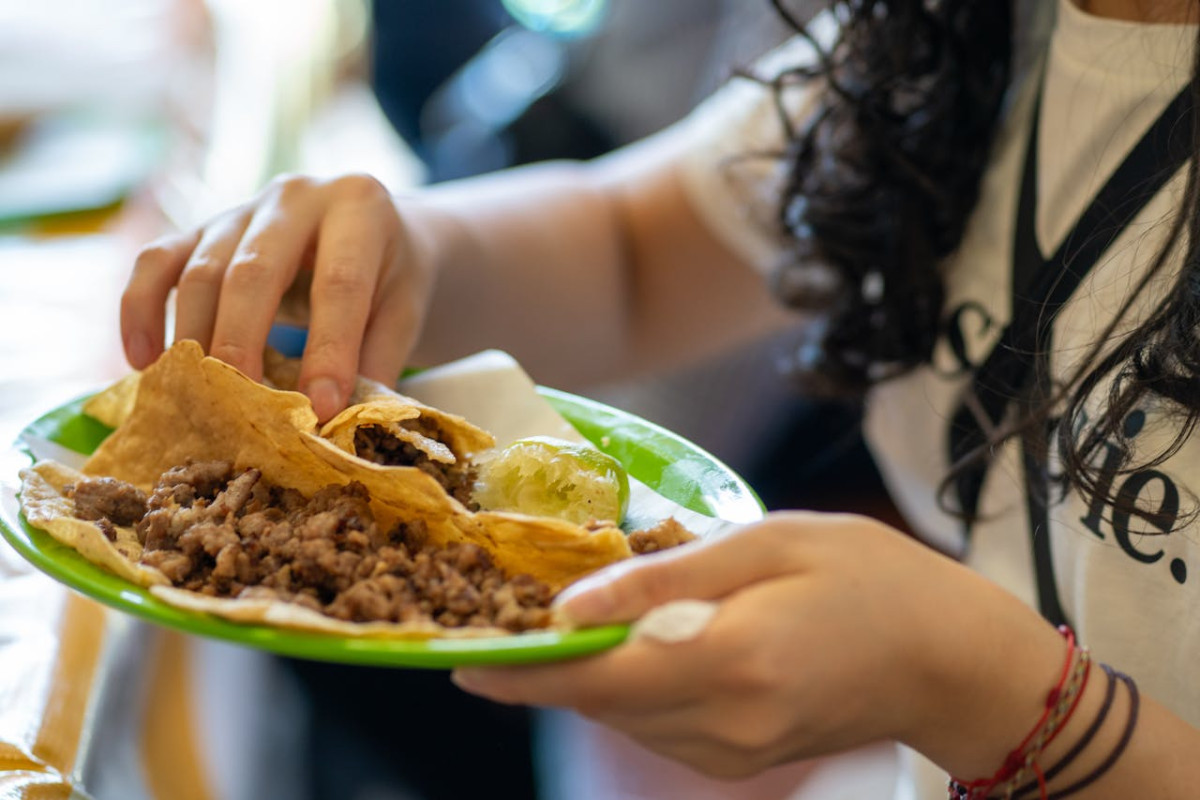 hands of woman holding plate and eating tacos