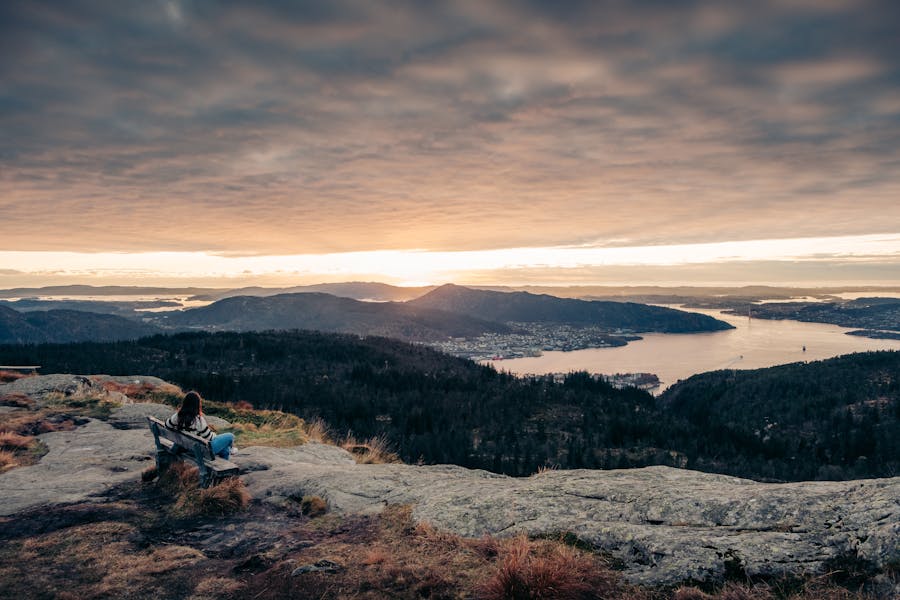 hiker sitting on a bench watching the sunset over the city of bergen from the top of rundemanen mountain